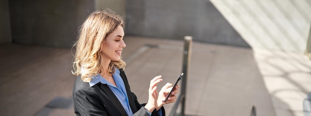 Бесплатное фото Портрет молодой деловой женщины на эскалаторе, использующей смартфон и улыбающейся нажимая на мобильный телефон