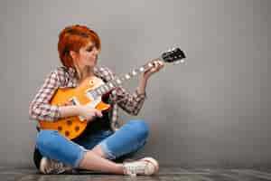 Бесплатное фото Портрет молодой девушки с гитарой на сером фоне.