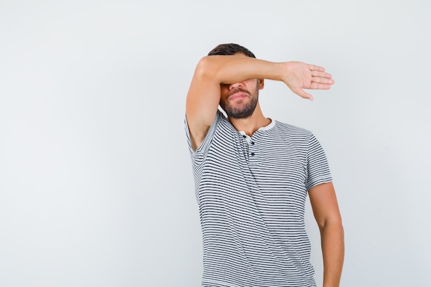 Портрет молодого человека, страдающего от сильной головной боли в футболке и выглядящего обеспокоенным, вид спереди