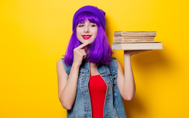 黄色の背景の本と紫色の髪型の若いスタイルの流行に敏感な女の子の肖像画