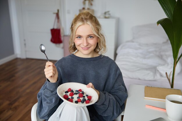 Бесплатное фото Портрет молодой создательницы контента-влоггера, показывающей свой домашний завтрак на камеру, съедая десерт