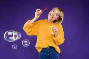 Бесплатное фото Портрет молодой женщины, пускающей мыльные пузыри над фиолетовой стеной