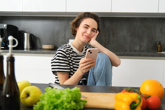 無料写真 近くに座っているスマートフォンを使用してオンラインで料理レシピを探している若い女性の肖像画