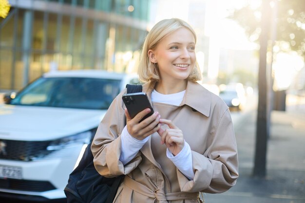 Бесплатное фото Портрет молодой женщины, использующей приложение для карт на смартфоне. студент с рюкзаком гуляет по улице.