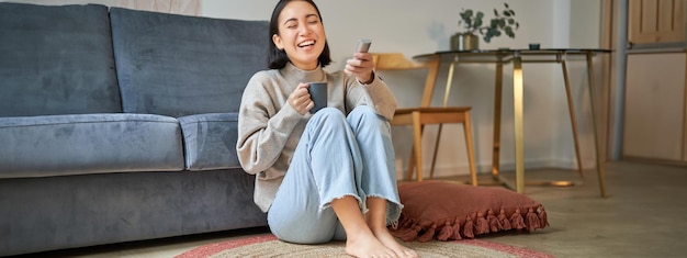 無料写真 床に座ってテレビでチャンネルを切り替えながらリモート視聴している若い女性の肖像画