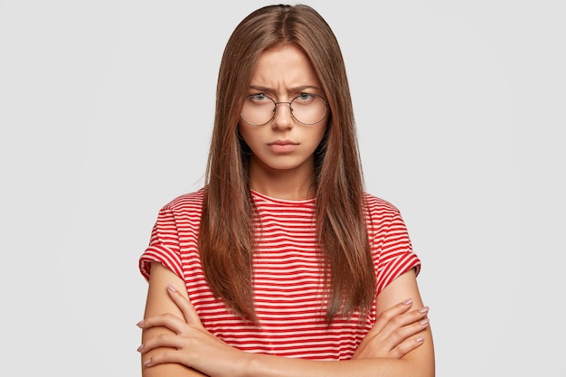 Portrait of offended angry woman stands in insulted gesture, has sulked face, keeps arms folded