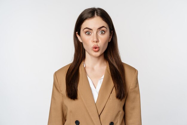 Portrait of office lady at workplace looking surprised and curious wow face standing over white back...