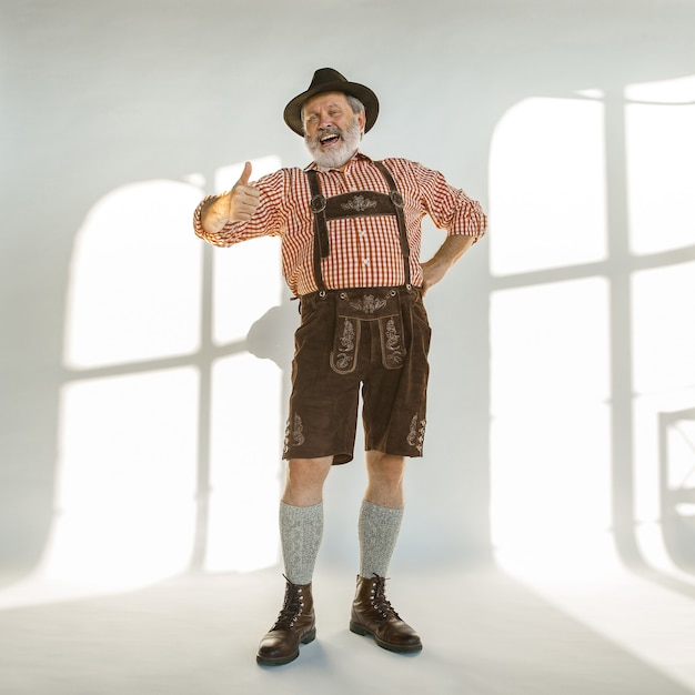 Portrait of Oktoberfest senior man in hat, wearing the traditional Bavarian clothes. Male full-length shot at studio on white background. The celebration, holidays, festival concept. Happy calling.