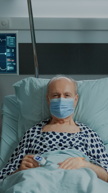 Free photo portrait of old patient with face mask sitting in hospital ward