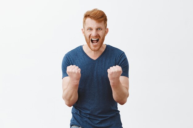 Portrait of outraged angry and pissed mature bearded redhead strong man, clenching fists near chest, shouting with anger and frowning, wanting punch offender