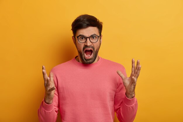 Portrait of outraged man stands in furious gesture, screams loudly