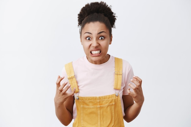 Portrait of outraged pissed and angry cute dark-skinned woman with afro hairstyle, clenching fists and staring with hate