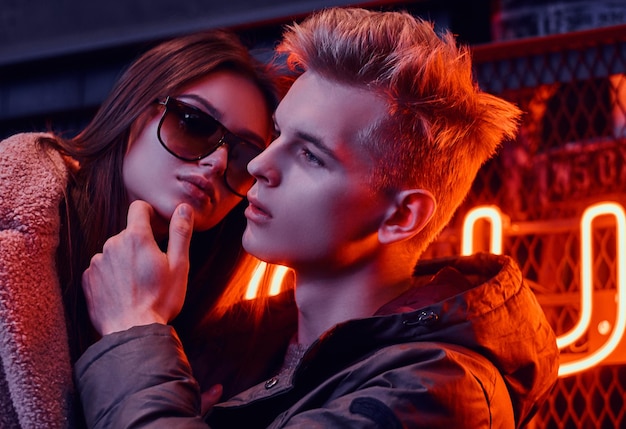 Portrait of a passionate young couple in the underground nightclub with industrial interior, he gently touches her chin
