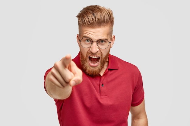 Free photo portrait of peevish bearded guy with ginger trendy hairstyle, yells angrily at somebody, points with index finger directly at camera