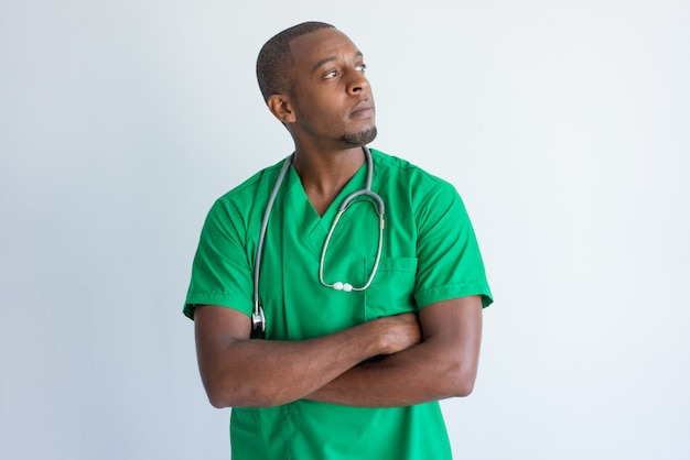 Portrait of pensive African American doctor standing with folded arms.