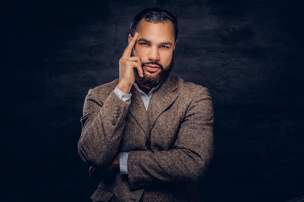 Foto gratuita ritratto di un uomo afroamericano pensieroso, vestito con una classica giacca marrone in piedi in uno studio su sfondo scuro.