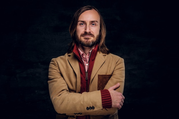 Portrait of pensive bearded hipster in jacket and red sweater on the dark background.