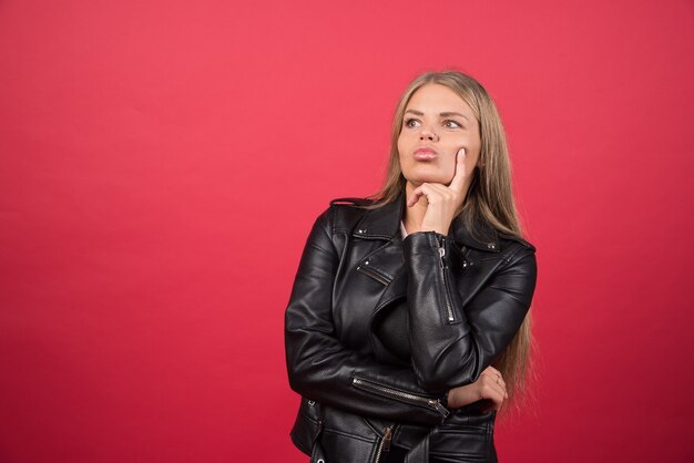 Portrait of a pensive woman standing and posing on a red wall