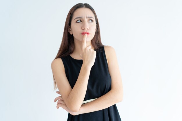 Portrait of pensive young Asian woman standing with hand on chin