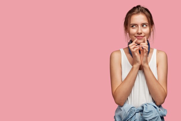 Portrait of pensive young woman with glasses posing against the pink wall