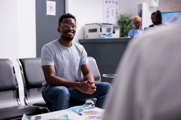 Portrait of person sitting in waiting area, having checkup examination appointment with physician to cure disease diagnosis. Young adult in waiting room at hospital lobby before consultation.