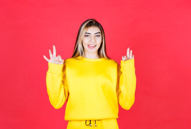 Портретное фото привлекательной девушки-модели с высунутым языком, показывающей жест ОК