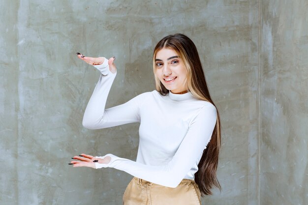 Portrait photo of a smiling girl model standing and showing large size with hands 