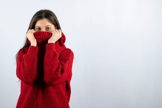 Portrait photo of a young woman model in red warm sweater covering face with collar
