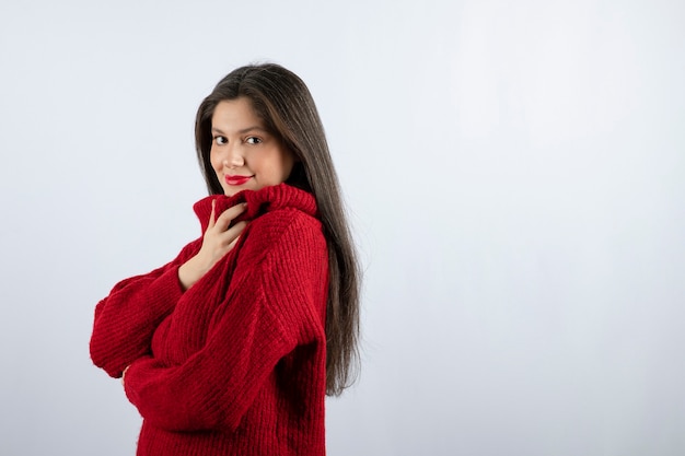 立ってポーズをとって赤い暖かいセーターの若い女性モデルの肖像写真