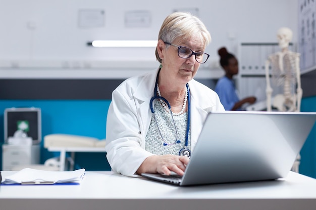 Foto gratuita ritratto di medico con stetoscopio utilizzando laptop per lavorare sull'assistenza sanitaria in clinica. medico donna che lavora con computer e tecnologia per eseguire l'analisi del trattamento di prescrizione per l'esame.