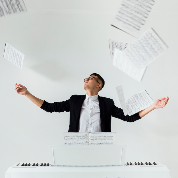 Free photo portrait of a piano player throwing the musical sheets in the air sitting against the white background