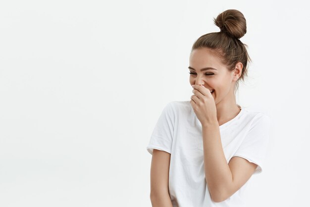 portrait of playful feminine caucasian woman laughing while looking at copy space and covering mouth with hand