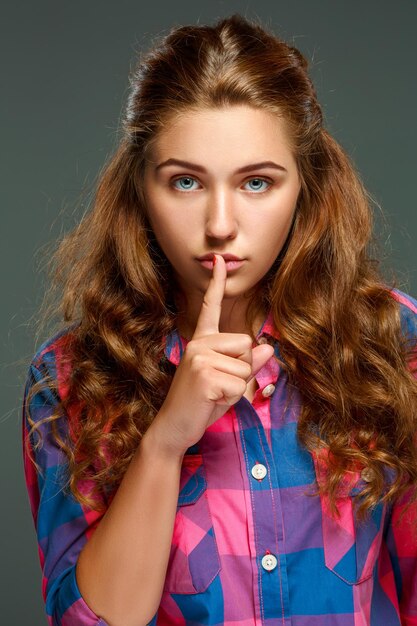 Portrait playful young brunette woman with wavy hair, looking at the camera, isolated on dark background