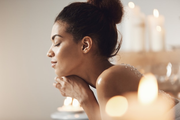 Portrait of pleased african woman relaxing with closed eyes in spa salon.