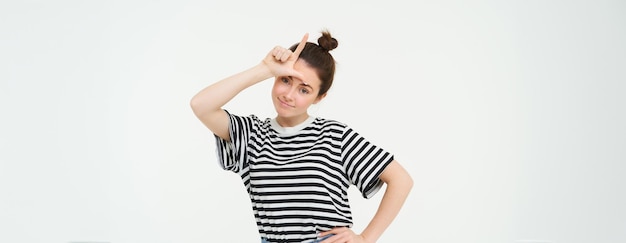 Free photo portrait of pleased arrogant young woman showing loser gesture l letter on forehead smirking