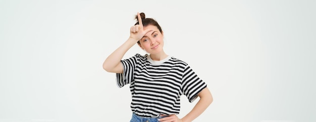 Free photo portrait of pleased arrogant young woman showing loser gesture l letter on forehead smirking