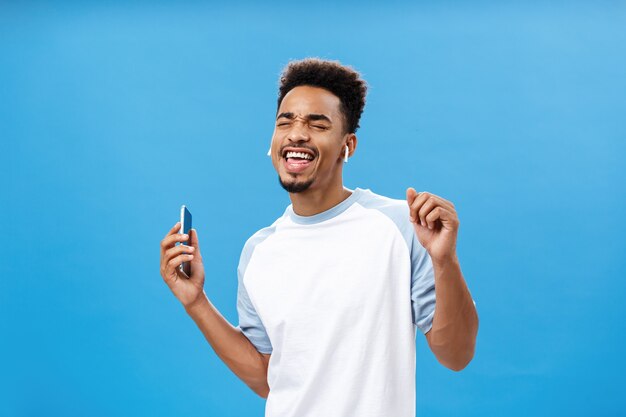 Portrait of pleased and carefree handsome stylish urban african american male in casual tshirt danci...