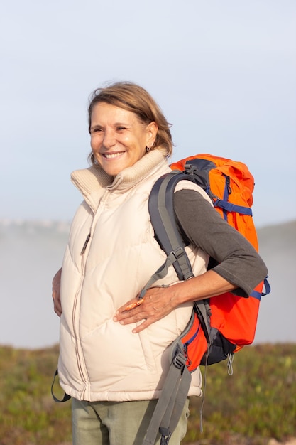 Free photo portrait of pleased elderly woman with backpack. sporty woman in casual clothes looking at camera with bright smile. sport, adventure, hobby concept