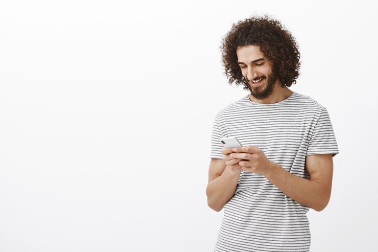 Free Photo portrait of pleased good-looking masculine guy with beard and curly hair, holding smartphone