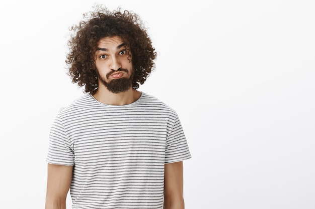 Portrait of plyaful carefree attractive male model with beard and curly hair, sticking out tongue and pouting, making funny faces