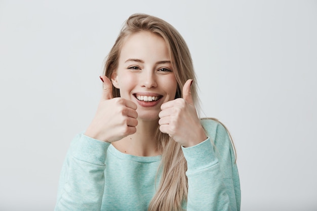 Portrait of positive blonde female woman with broad smile and thumbs up