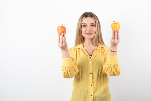 Portrait of positive girl holding colorful bell peppers on white wall.