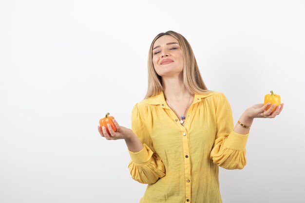 Portrait of positive girl holding colorful bell peppers on white wall.