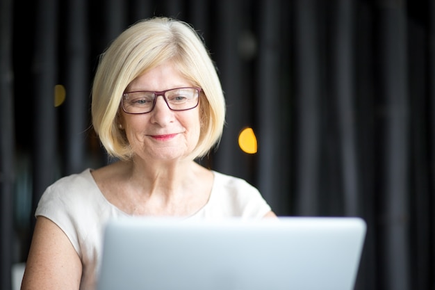 Free photo portrait of positive senior woman using laptop