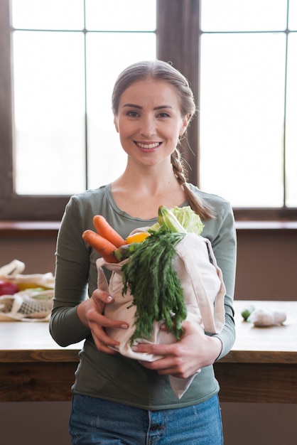 Портрет положительной молодой женщины, держащей органические овощи