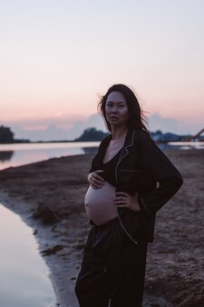 Portrait of pregnant woman on beach romantic photo of attractive young brunette in unbuttoned dark p...