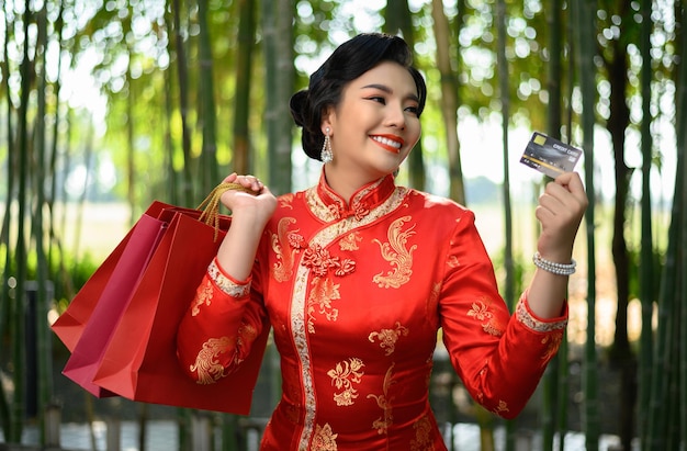 대나무 숲에서 행복과 함께 쇼핑백과 신용 카드를 손에 들고 중국 치파오에 초상화 예쁜 아시아 여자