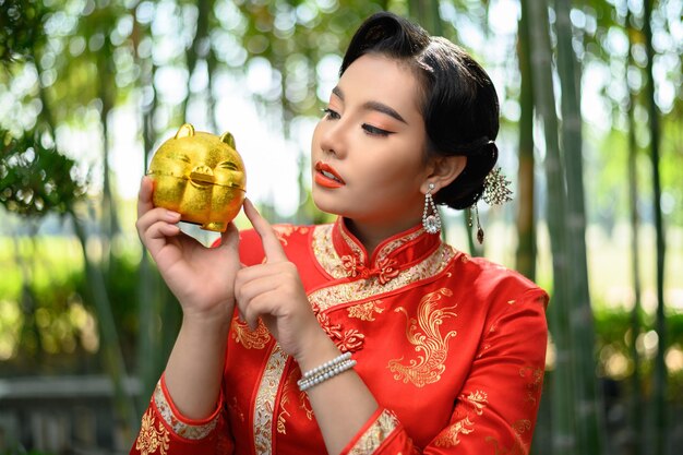 貯金箱と竹林の人差し指でポーズをとる中国のチャイナドレスの肖像画きれいなアジアの女性