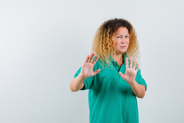 Portrait of pretty blond lady showing refusal gesture in green polo t-shirt and looking disgusted front view