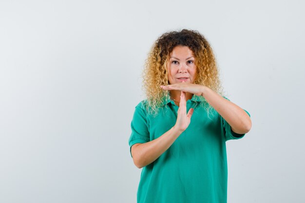 Portrait of pretty blond lady showing time break gesture in green polo t-shirt and looking confident front view